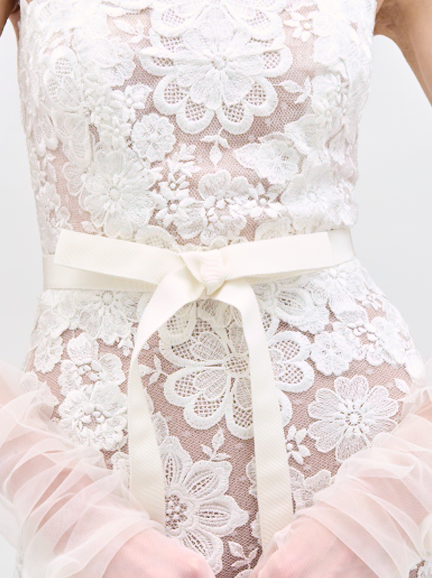 Close-up of a white lace dress with a bow detail on a plain background