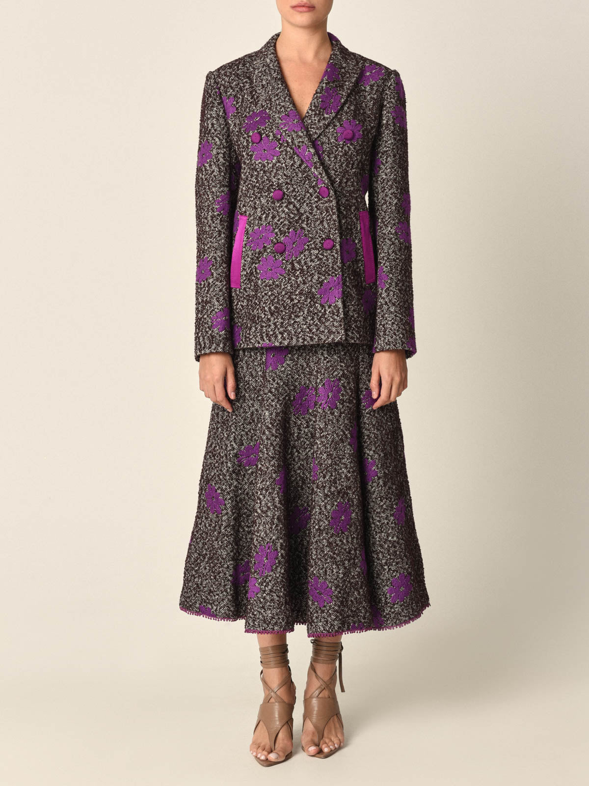 The Casilde Cape Violet is a brown textured cape adorned with violet gray floral embroidery, featuring a front tie closure with multi-color tassel details.